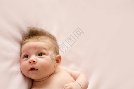 头发可爱的两个月大女婴躺在粉红色毯子背上婴儿快乐的眼睛盯着高清图片素材