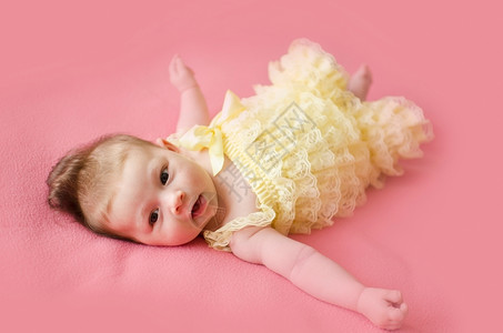 黄色的可爱两个月大女婴躺在粉红色毯子背上头发白种人眼睛盯着高清图片素材