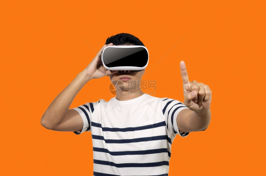 有虚拟现实头盔的年轻人站在橙色背景的室内青年拿着虚拟现实头盔的年轻人未来视频一种图片