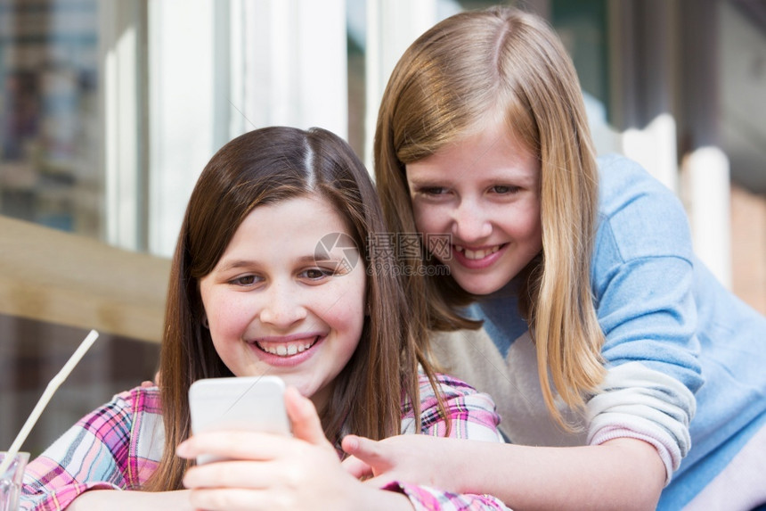 社会的两名在咖啡厅年轻女孩通过移动电话阅读短信移动的息图片