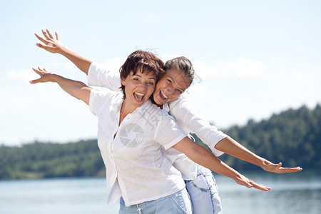 快乐的微笑母亲和女儿在阳光夏日的水景中玩小猪游戏家庭海女孩图片