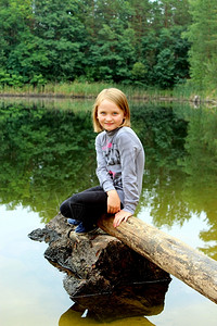 生活美丽的女孩坐在河边原木上小美丽的女孩坐在河边原木上经过孩子图片