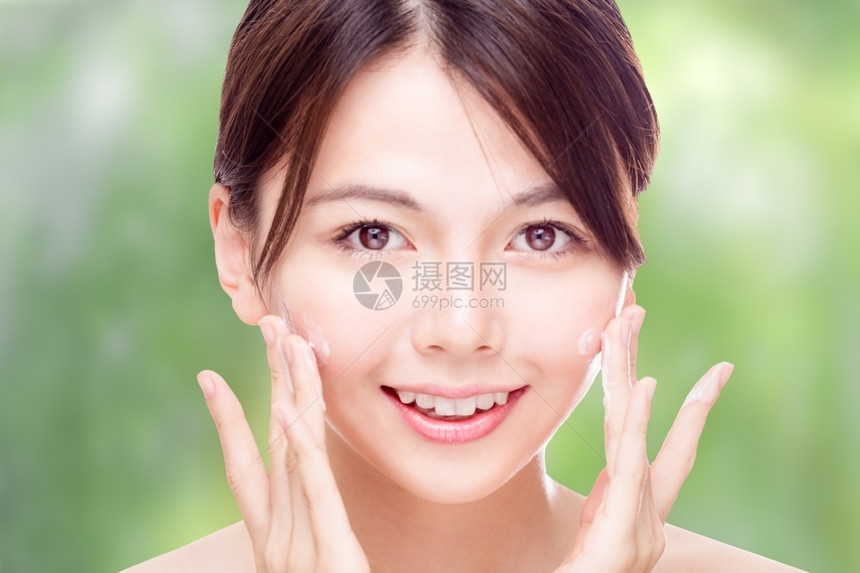 美貌的女子在绿色背景模糊的情况下用奶油来面对皮肤护理概念脸颊健康美丽的图片