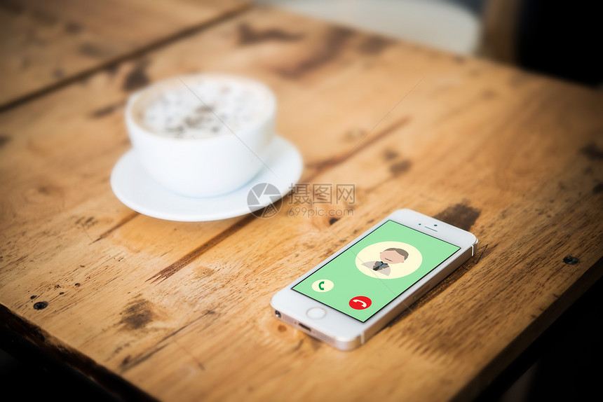 咖啡店应用在木制咖啡桌上用一杯的智能手机在屏幕上呼来电社区人民概念办公室图片