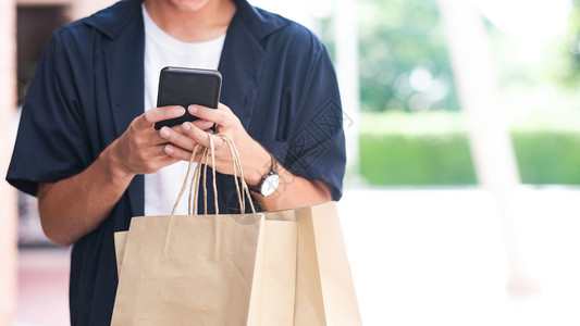 商业购物中心快乐的有购物袋青年男子在购物时使用手机购买移动电话图片