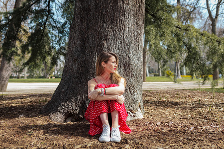 女孩选址身穿红长裙坐在树边的金发年轻姑娘吸引人的图片