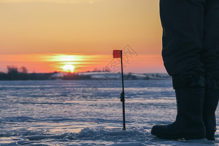 坐着身体寒冷的冬天日落在湖边的渔民图片