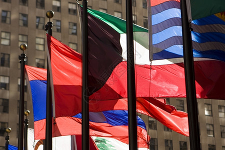淡彩风在纽约市洛克菲勒中心的旗帜展厅阳光明媚一天在风中狂野挥舞着许多明亮和彩的旗帜视窗办公室国民背景
