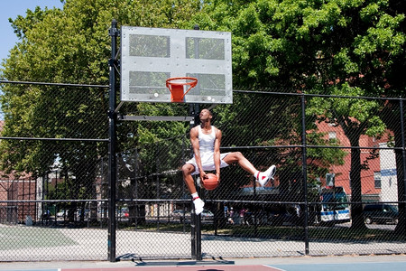 篮球衣身穿白色空中跳跃的衣运动健壮英俊的非裔美国人男子在暑日户外法庭上打篮球时身着赤地从空中飞到篮子前同时在户外法庭打篮球夏天乐趣为了背景