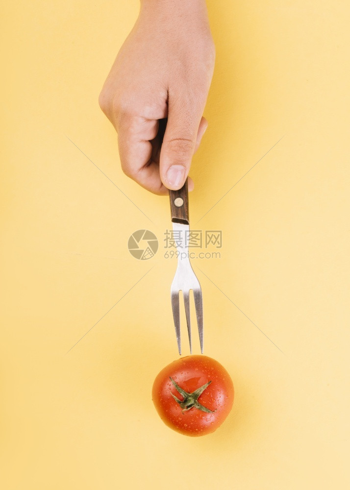 酸奶框架插入叉子红番茄黄色背景的人类手图片