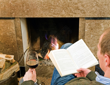 男人在壁炉边读书喝杯酒放松保持牛仔裤羊毛温暖的高清图片素材