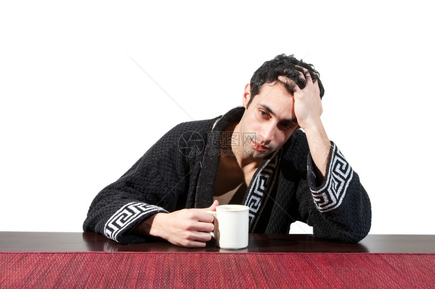 琢磨早上的帅有压力家伙刚醒来时他过坐在一张桌子上穿着长袍用杯子坐在一个桌上手伸着头发在白边被孤立英俊的图片