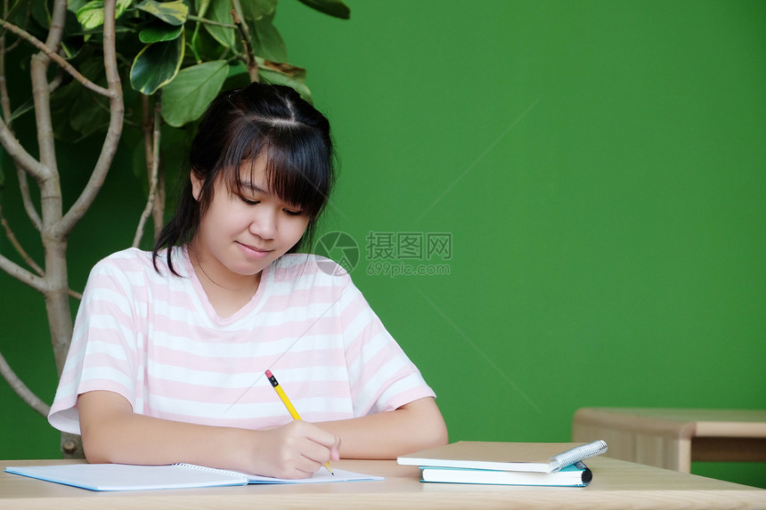 亚洲青少年女学生带着微笑的面容在课堂上桌写笔记本纸教育概念亚洲青少年女学生在家工作士室内图片