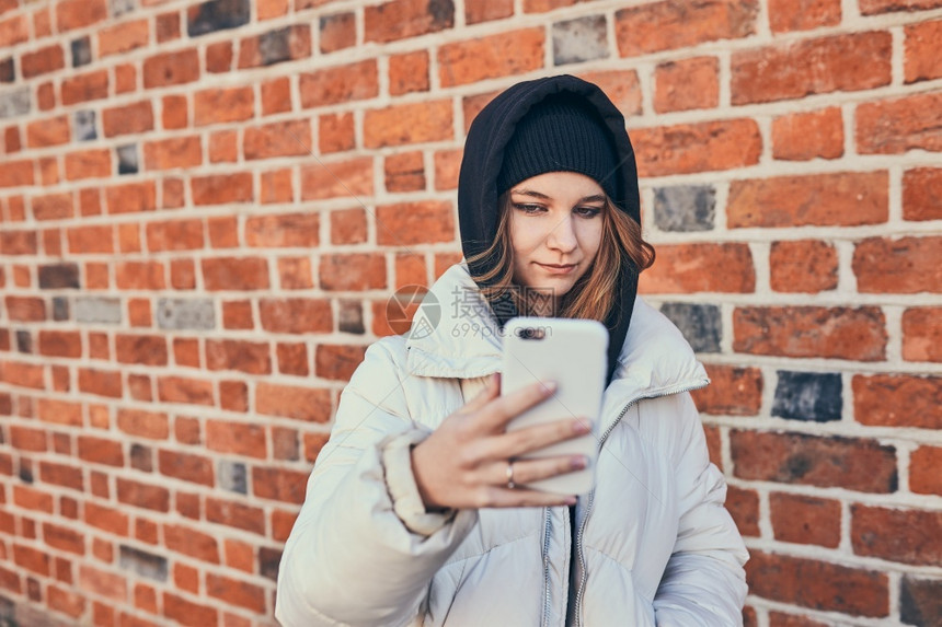 聊天保持观看年轻女子有视频电话远程交谈拍自照片手持智能机站在砖墙上图片