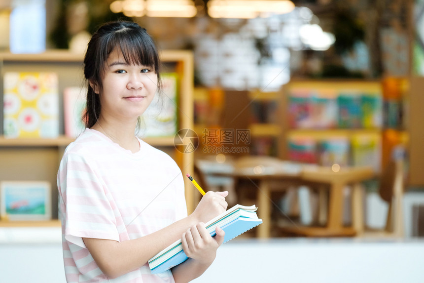 站在模糊图书馆背景前手拿书本的女学生图片