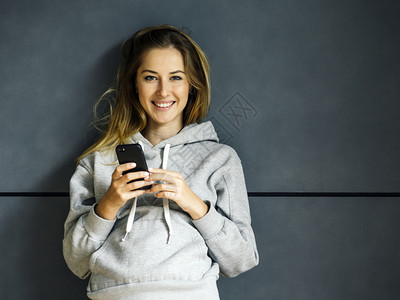 幸福相机照片中一位美丽的金发年轻女子仰靠墙壁微笑使用手机时着微一种图片