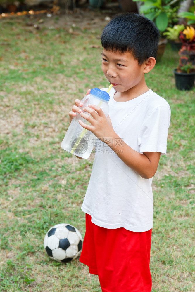 亚洲人蓝色的泰国男孩用稻草喝来自糖瓶的冷水图片