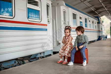 快乐的旅行在小火车站穿着旧衣服和式手提箱的男女小孩和少游客背景