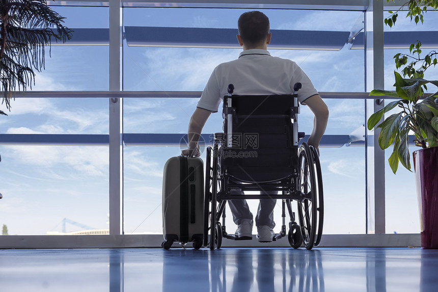 飞男人坐在轮椅的年轻人和行李在机场特关上恢复图片