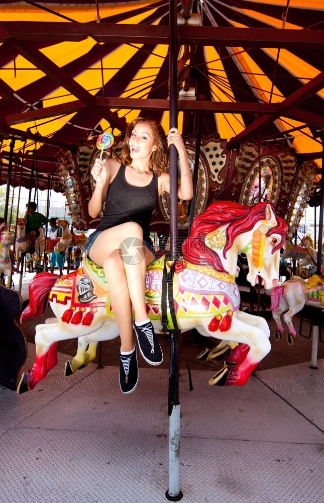 在科尼岛嘉年华狂欢节主题公园骑着旋转木马快乐的笑女骑马衬衫可爱的女士图片