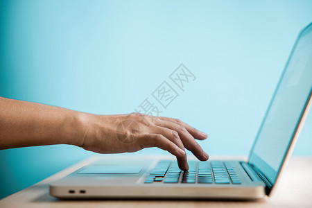 男人点击计算机键盘侧视图近镜头和有选择地关注使用笔记本电脑在桌边工作反对蓝墙清洁和最小照片的手指人Choptop男互联网背景图片