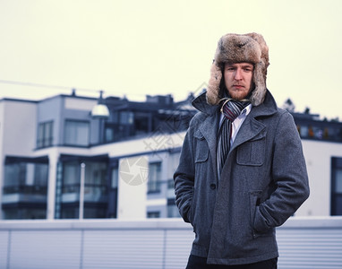 一个男人穿着毛皮帽和温暖的外套公寓大楼的背景摆姿势灰色的时髦图片