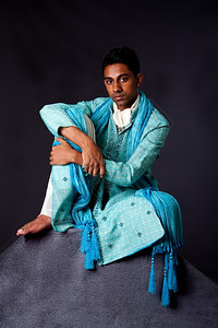 轻松婚姻印度教穿着轻蓝色的Dhoti和披肩装饰的印度男子身着典型民族新郎服饰的美丽而纯正印度钦都男子坐在仰靠着膝盖的石头上放松地背景图片