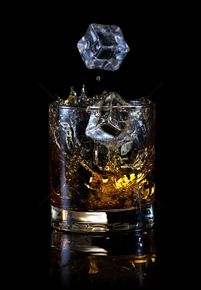 喝鸡尾酒飞行冰的立方体落在玻璃威士忌里孤立在黑色背景冰的立方体上倒在玻璃威士忌里图片