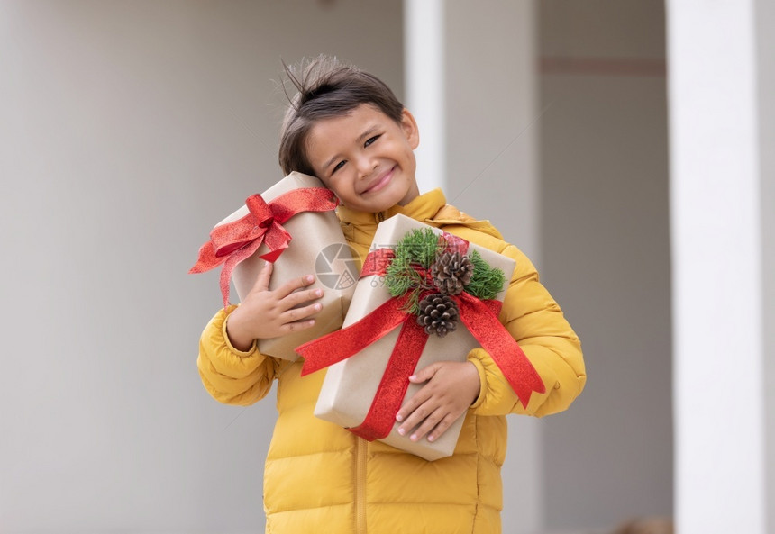 购物一个穿着冬大衣的可爱男孩拿着礼物盒微笑为圣诞节做准备衣服外套图片