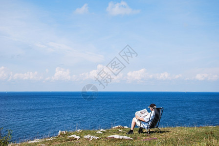 坐在椅子上的人海边阅读报纸上瑞典波罗的海风景美观波罗地海BalboreSeainSweden坐着男人经过背景