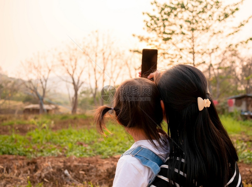 成人亚洲小女孩在日落背景下和母亲一起在花园里拍照的背影但父母公园图片