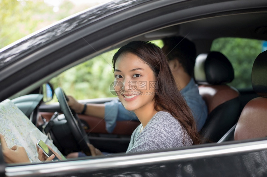 窗户里面外使用智能手机和的亚裔女及男子驾驶汽车进行公路旅车内有的幸福年轻夫妇图片
