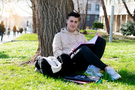 坐在草地上的青年靠着树学习图片