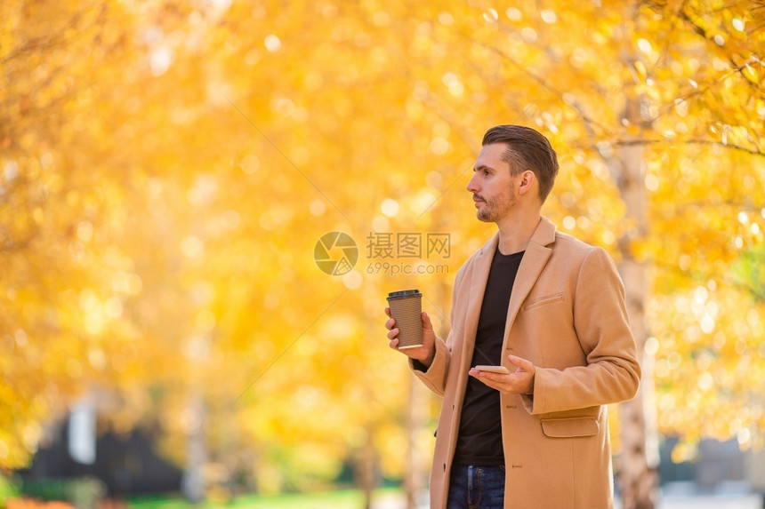 木头快乐的温暖秋天在公园户外与咖啡一起穿大衣的快乐男子青年图片