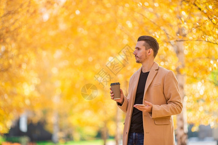 木头快乐的温暖秋天在公园户外与咖啡一起穿大衣的快乐男子青年图片