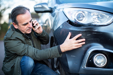 驾驶者户外意用手机打电话给保险公司后汽车受损的不开心成熟男司机破坏图片
