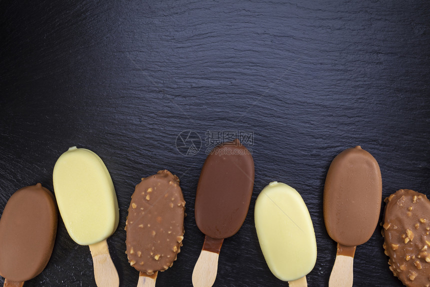 奶油棒糖冰淇淋贴在木棍上黑石块板的巧克力覆盖着冰淇淋粘在黑色的巧克力上美味图片