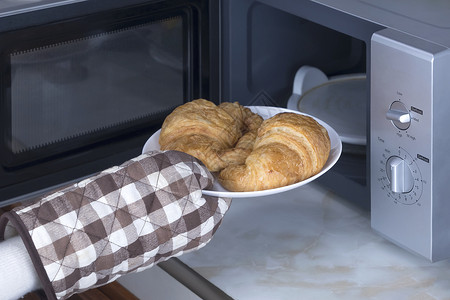 一顿饭白色的牛角包女手戴耐热套在厨房从微波炉中取羊角面包图片