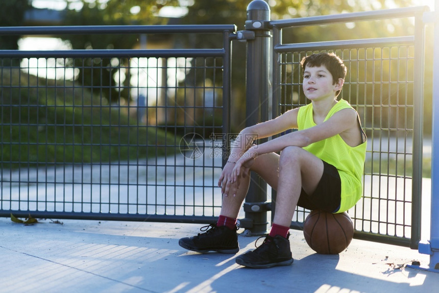 一个年轻的户外坐在街头球场的篮上年轻户外坐在街头球场的篮上带着金属的水平孩子们图片