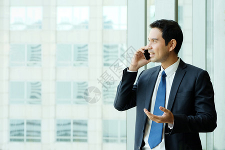 商人通过窗户城市观视办公室建筑内部背景商人电话交谈智能商业人讲智能电话领导者专业的称呼成熟高清图片素材