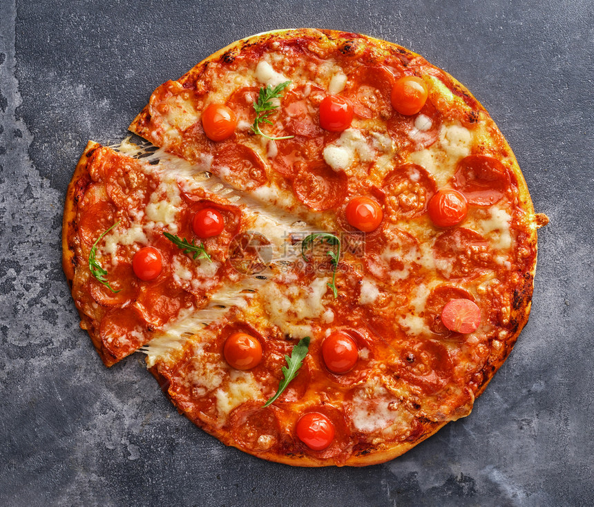 意大利语灰石背景上的辣椒尼比萨片和樱桃西红番茄在灰石背景上切成美味的辣椒尼披萨餐厅快速地图片