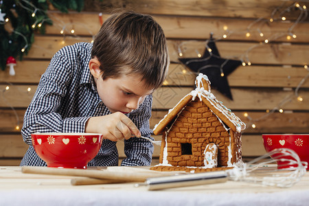 人们喜庆的一种位年轻男孩在圣诞节前家里装饰姜饼屋的照片他写道图片