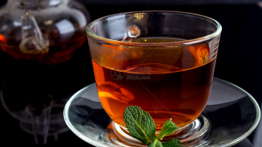健康杯子茶和黑玻璃上薄荷叶杯茶和黑背景上薄荷叶的商业图片
