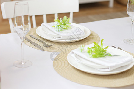 盘子椅木制的白色桌餐上为两个人设置的美食圆餐巾眼镜和具上配有人造花板树枝高清图片素材