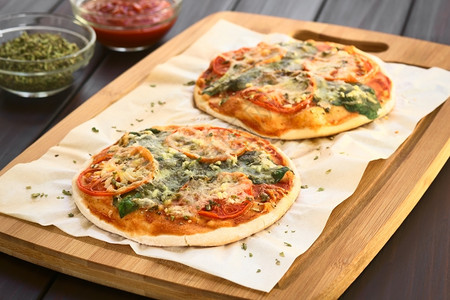 自然蔬菜木板上烤纸的自制菠菜和番茄披萨用天然光聚焦点在暗木上拍照第一张披萨的焦点是三分之一烘烤背景图片
