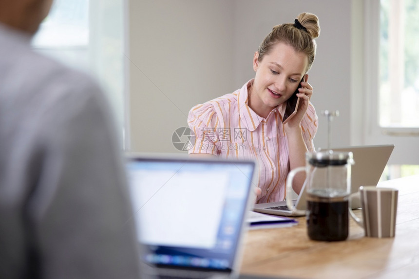 女士商人使用移动电话在大流行禁闭期间从家中坐在桌边工作的夫妇企业联合工作称呼图片