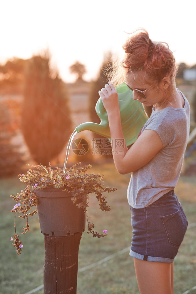 能够帮助为花盆里种植的鲜浇水从绿罐中倒在日落Candid人后院工作真实时刻和情况提供饮用水的少女夏天真实图片