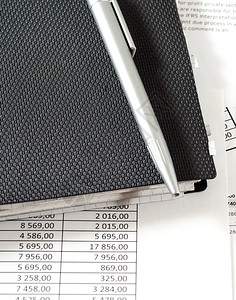 写金融带有财务表格和文件的上一张黑纸条的银笔面有财务表格和单据财务表格注纸和桌子上的笔黑色背景图片