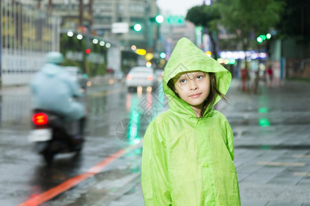 可爱的户外美丽穿着绿色雨衣在市街旁边淋雨的年轻女孩图片