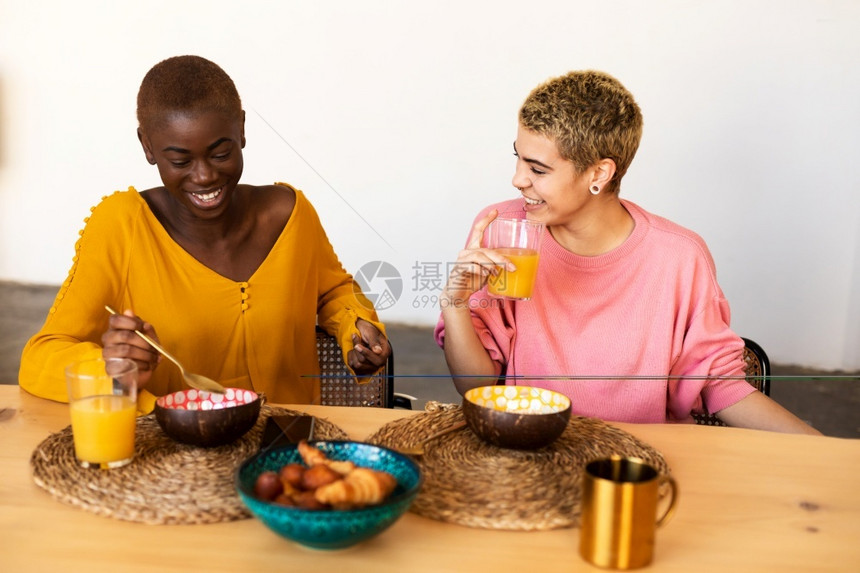 团结家庭多族裔快乐的一对多族裔夫妻在家放松同时吃早餐多族裔年轻夫妇在家休息同时吃早餐幸福的多族裔年轻女夫妇在家里放松享受图片